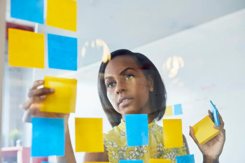 Young woman in office, sticking sticky notes to glass in office